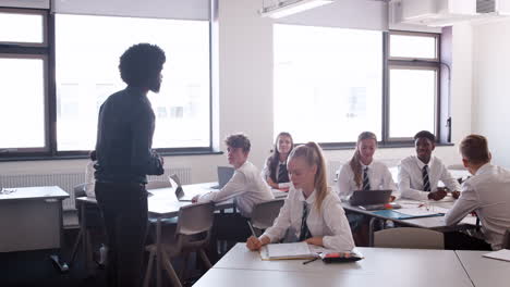 Profesor-De-Secundaria-Masculino-De-Pie-En-El-Aula-Enseñando-Lecciones-A-Alumnos-Uniformados-Que-Hacen-Preguntas