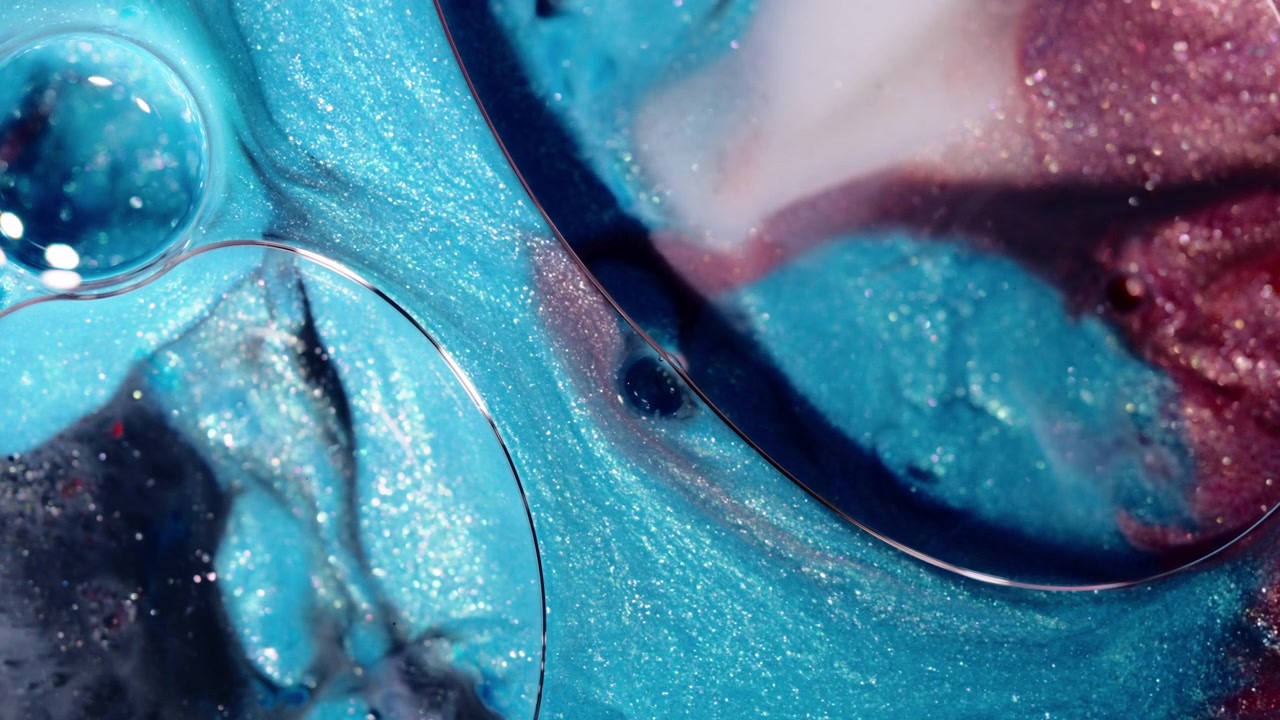 Turquoise and magenta shimmer pigments flow and form organic cell shapes in a close-up ink reaction shot.