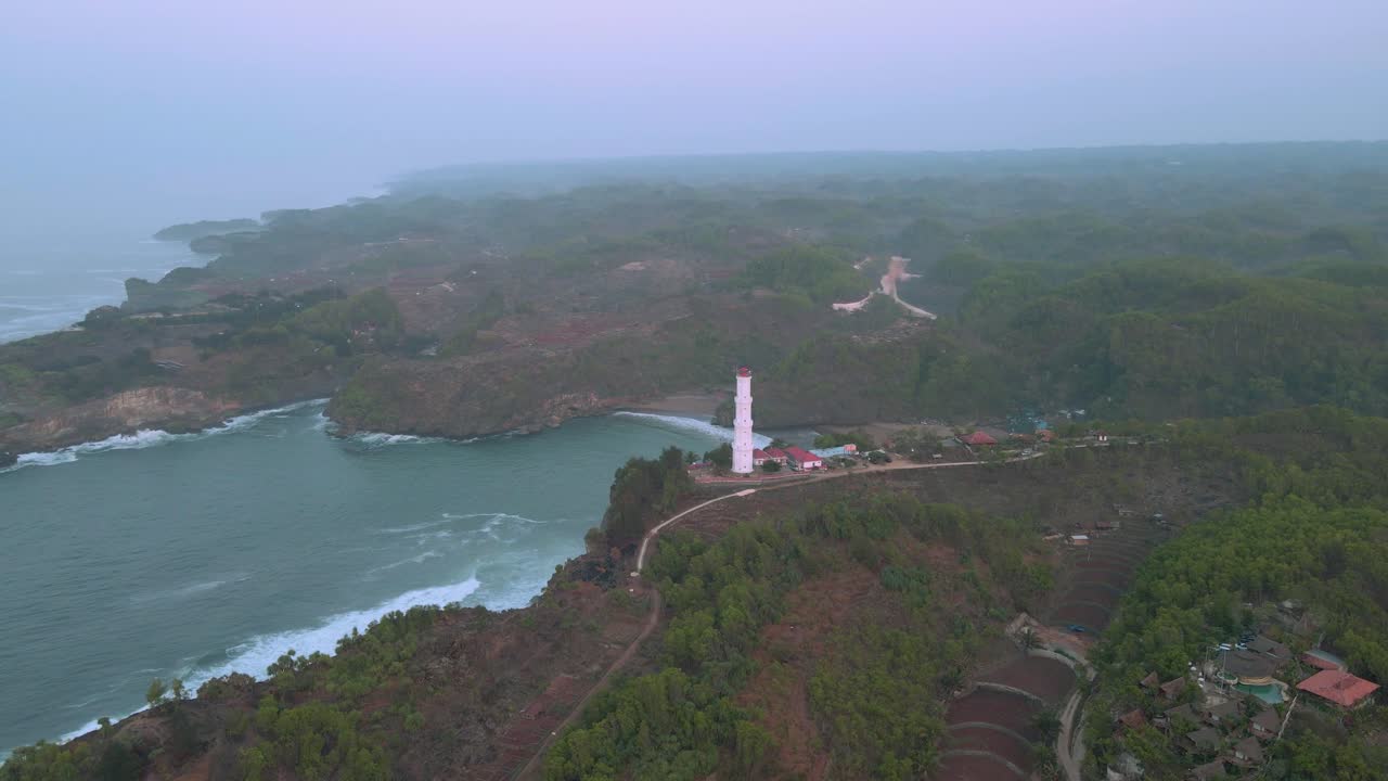 tomada aérea de órbita del faro en la playa de baron durante un día de niebla, indonesia