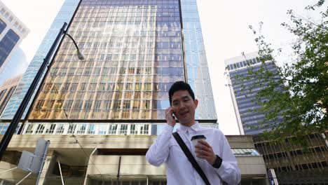 Man-with-coffee-cup-talking-on-mobile-phone-on-street-4k