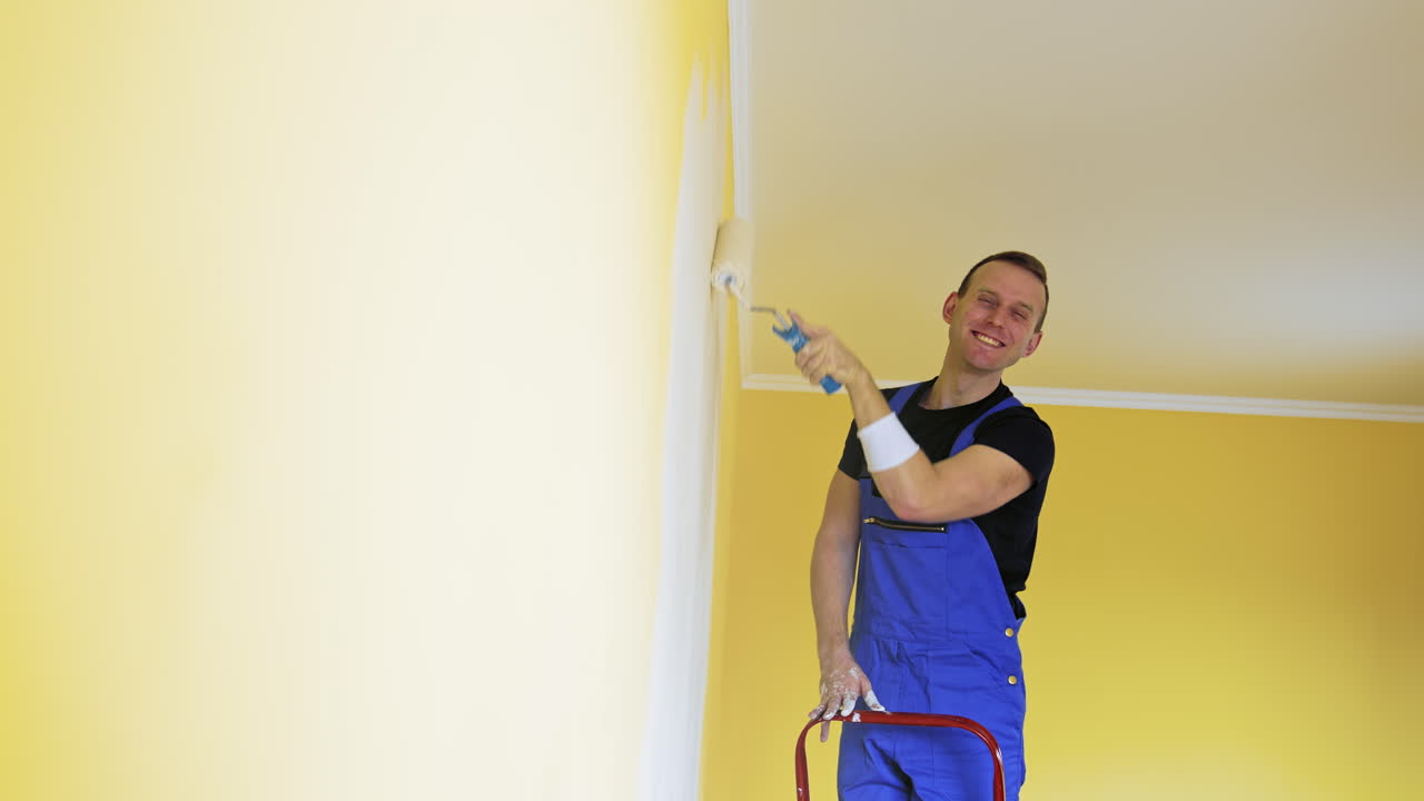 Man in work overalls paints the wall. Workman in the uniforms painting the walls with paint roller