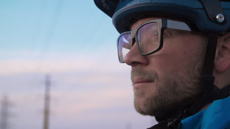 close up shot of a male mountain biker, atop a hill observing a town skyline as the low-sun creates a dramatic sky and serene setting