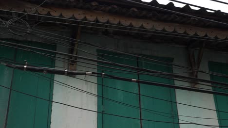 toma panorámica de un sistema de cableado desordenado en una aldea rural contra un edificio blanco con persianas verdes