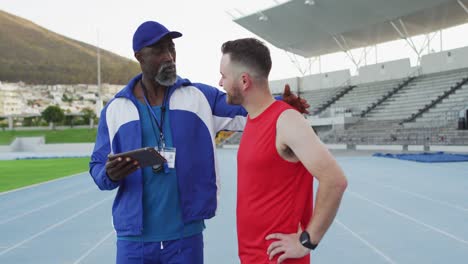 entrenador masculino afroamericano y atleta caucásico hablando durante una sesión de entrenamiento