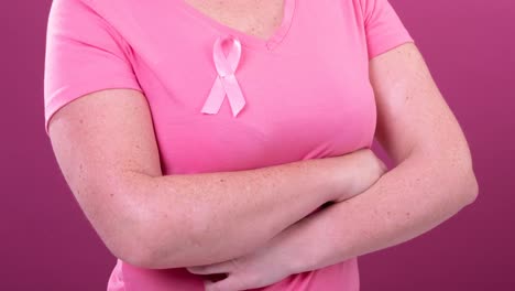 Video-of-midsection-of-caucasian-woman-wearing-pink-cancer-awareness-ribbon,-with-pink-background