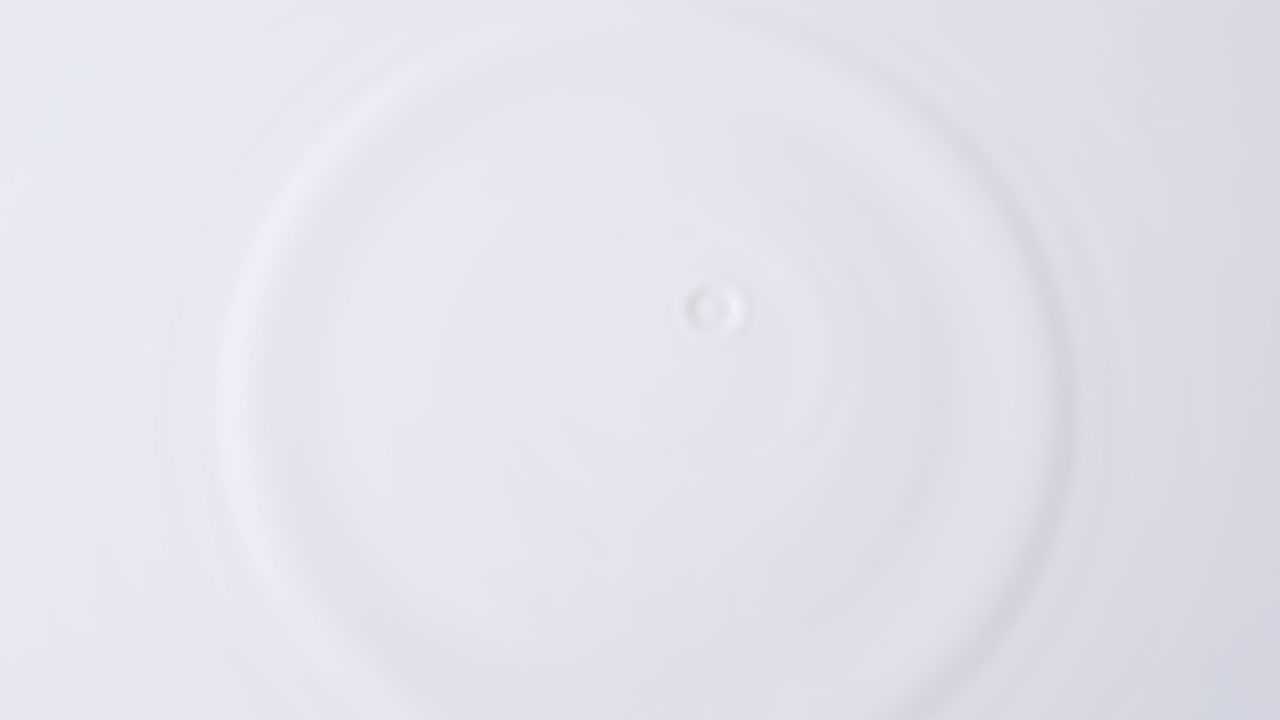 우유의 물방울은 밀크의 단단한 표면에 위에서 중앙으로 떨어집니다. 방울이 떨어지는 우유의 배경, 스피드 램프 효과의 4k 원시 느린 동영상 비디오, 고속 영화 카메라에서 촬영, 1000fps.