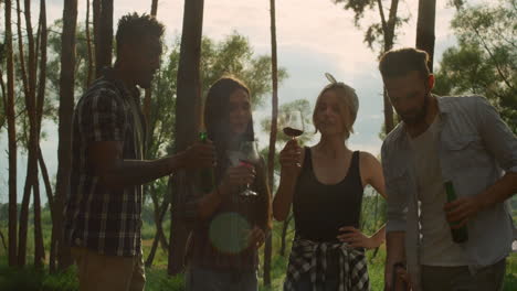 multiracial guys clinking glasses on backyard. friends relaxing in summer forest