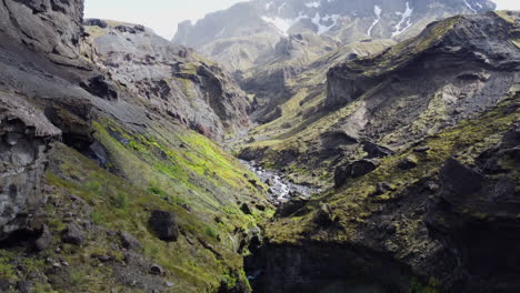 Aerial-shot-of-a-narrow-ravine-revealing-a-stream-flowing-on-the-rocks-alongside-cliffs