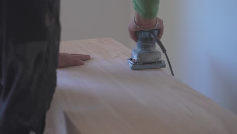 un primer plano de un hombre lijando el borde del avión de madera con una lijadora eléctrica