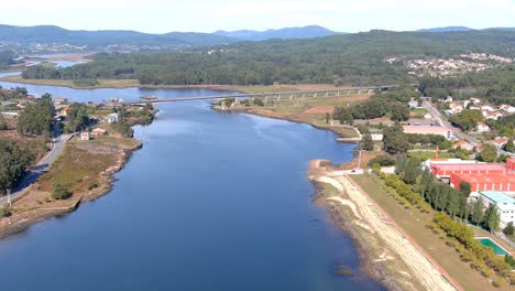 bridge over the ulla river with small industrial areas on the sides and the ruins of the castle towers of the viking landing, sunny afternoon, drone shooting traveling forward