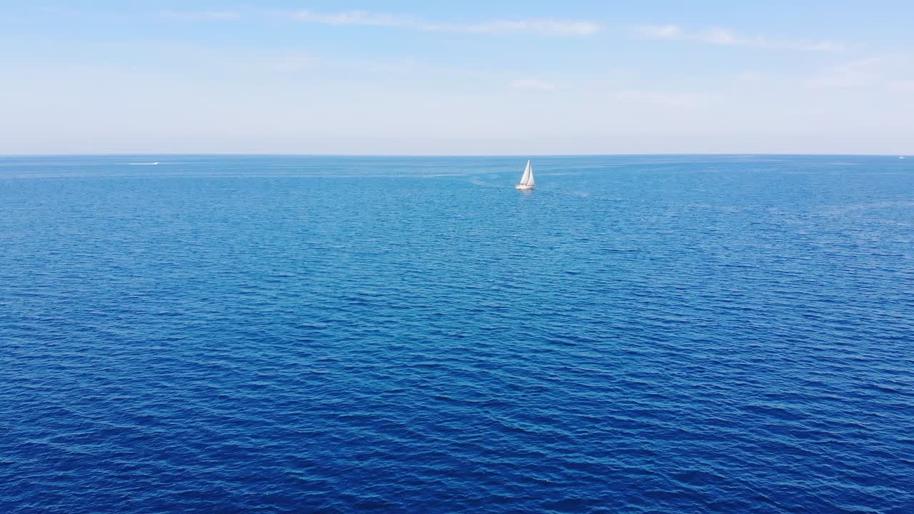 Lonely white sailboat sails in the distance of the bright blue ocean. Drone aerial view
