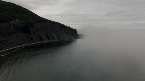 drone descends through cold foggy ocean mist to reveal dark mountain and cliffy coast line