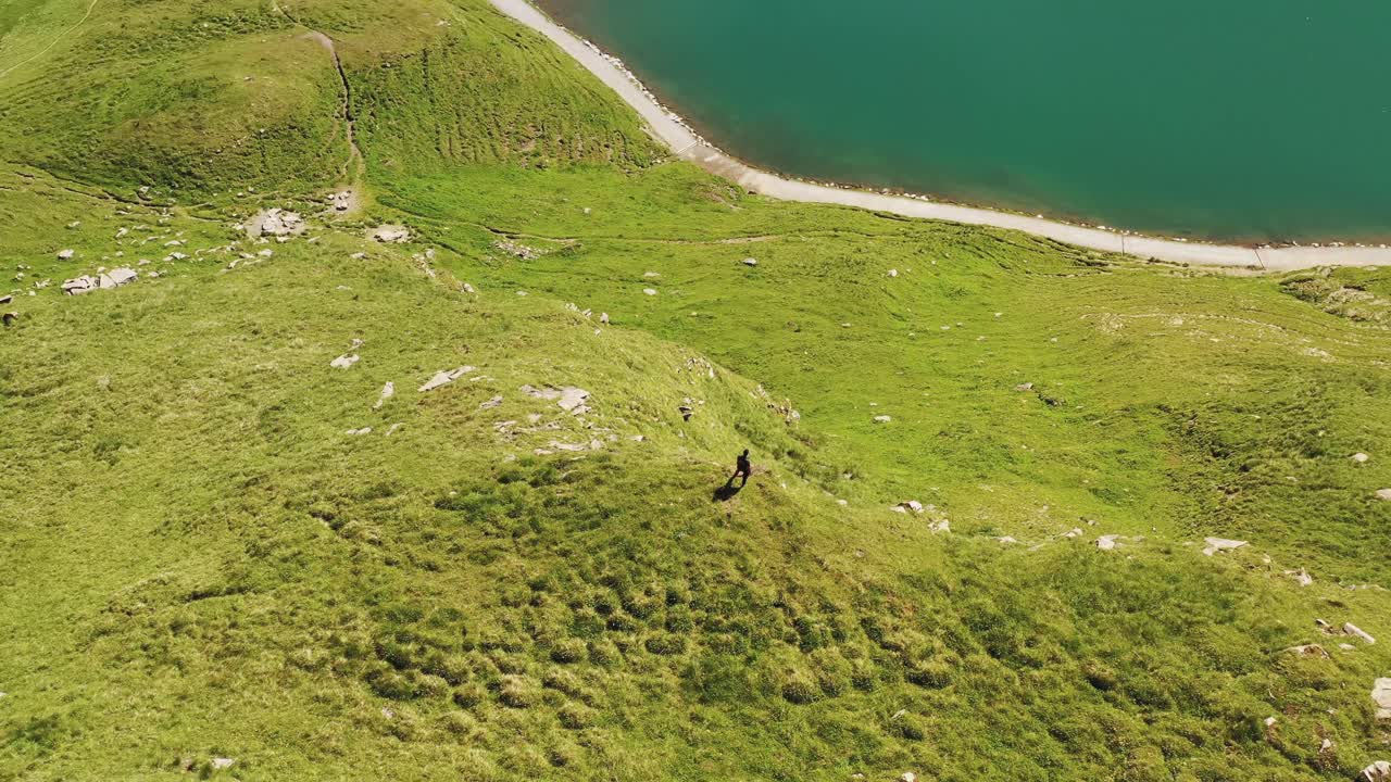tomada de órbita aérea: excursionista caminando por un verde prado cubierto borde de la montaña con vistas al bachalpsee sendero del lago turquesa alpino en las montañas de los alpes suizos de grindelwald, suiza en verano