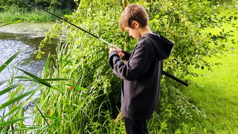 4k 60fps boy fishing coarse fishing in pond removing weed from fishing hook - handheld shot