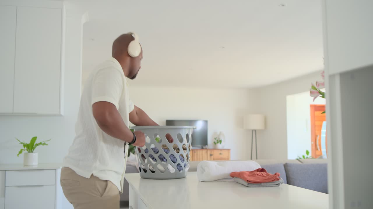 African American adult man pulling garments from laundry basket, folding on kitchen island to tidy