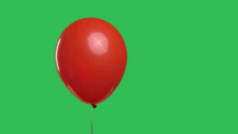 red oval shaped balloon hanging in the air against the background of a green screen chroma key. close up of colorful helium balloon. birthday, party decoration, holiday, surprise, gift. slow motion