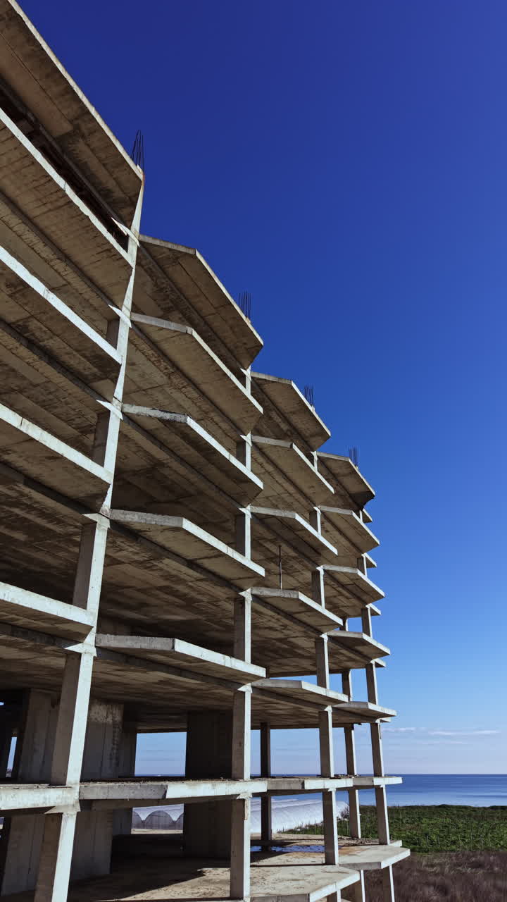 Construction progress of an unfinished building near the coast under a clear blue sky during the afternoon light