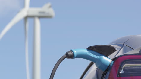 primer plano: un coche eléctrico sin marca se carga frente a una turbina eólica, día soleado