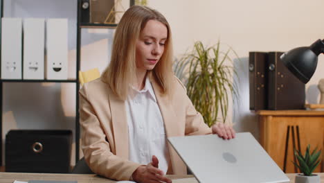 young business woman sitting at office workplace desk closing laptop pc after finishing remote work