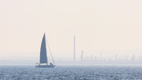 sailboat gliding across sea with industrial backdrop