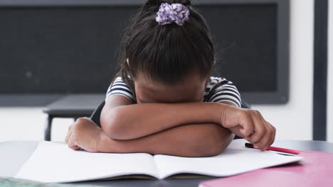 en un aula de escuela, una joven afroamericana apoya su cabeza en sus brazos