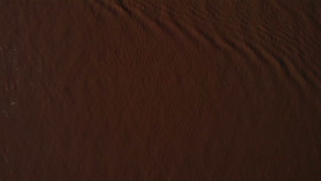 Aerial-Birds-Eye-Looking-Down-At-Ripples-Across-Brown-Coloured-River