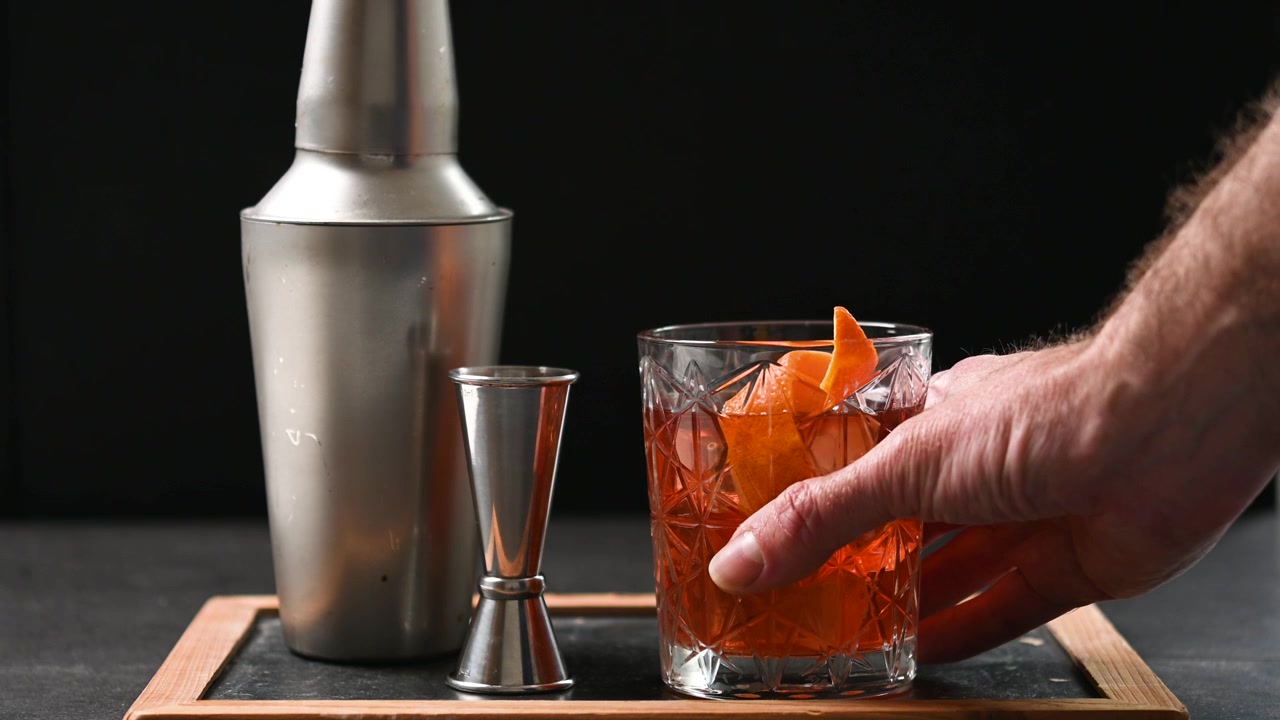 Mano che afferra un cocktail Old Fashioned su sfondo nero