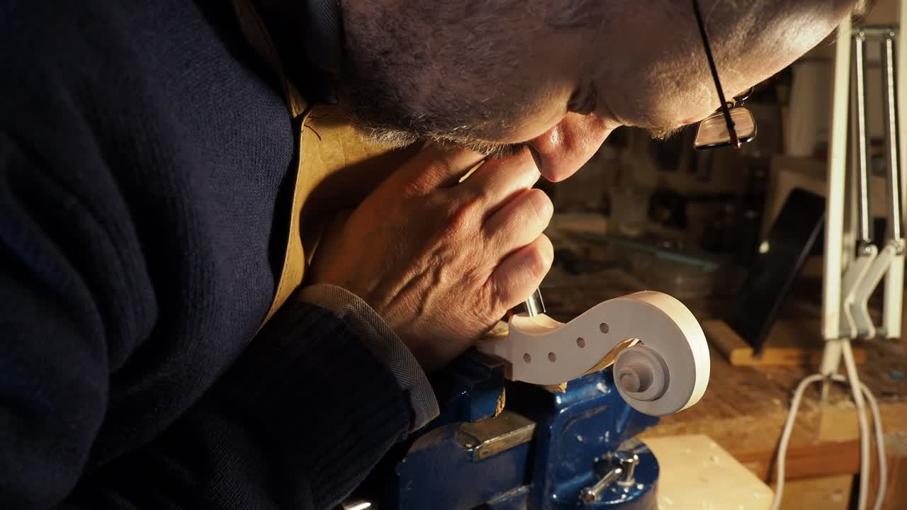 Luthier is bent over his work, demonstrating the meticulous focus and precision required in classic Italian violin making, delicately guide a chisel along the volute of unfinished scroll