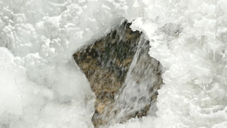 an abstract nature shot of a close up of fast flowing white river water passing beneath an opening in the frozen surface ice along the niagara escarpment, ontario, canada