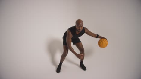 full length studio shot of male basketball player dribbling and bouncing ball against white background