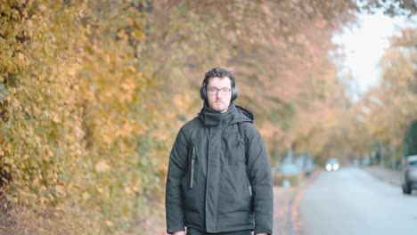 stylish european man with a beard and glasses leisurely strolls the autumnal suburbs of munich, deeply immersed in melodies from his headphones, absorbing the seasonal tranquility