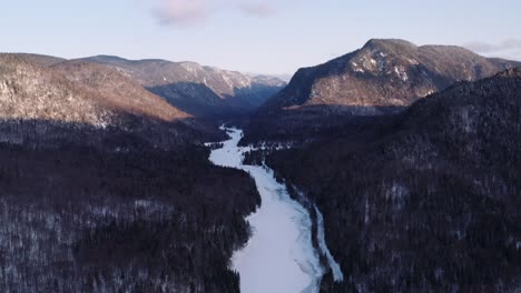 Toma-épica-De-Paisaje-Amplio-Aéreo-En-Movimiento-Hacia-Atrás-Del-Río-Nevado-Que-Fluye-A-Través-Del-Fiordo-Hacia-El-Valle-Del-Bosque-Boreal-Invernal