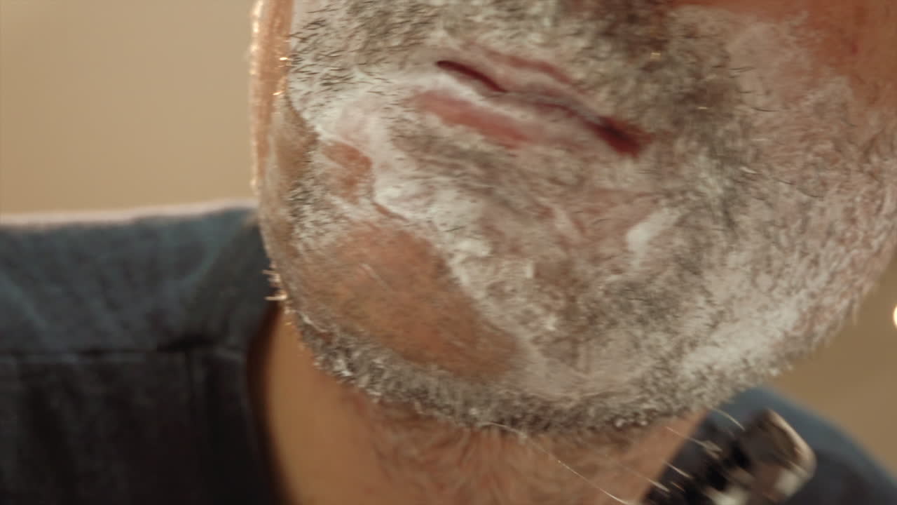 Close up of a man shaving his beard with a green and black razor