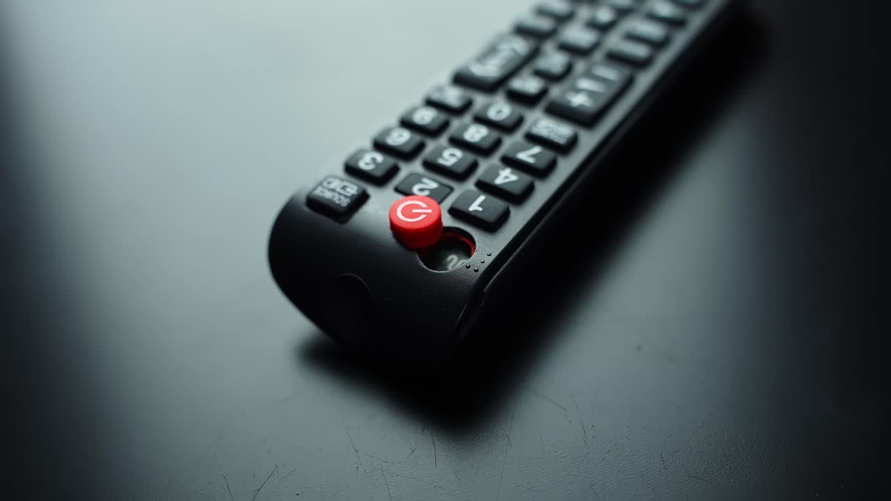 Broken TV remote with loose power button and damaged casing on dark tabletop. Shallow depth of field and copy space for repair, tech support, streaming, and home entertainment