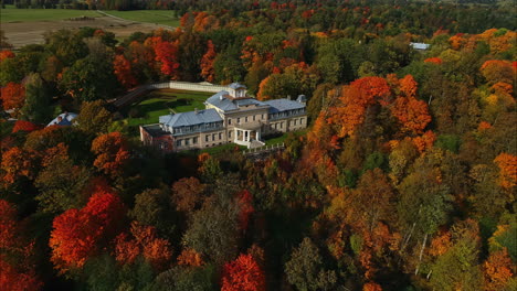 Luftdrohnenaufnahme-Eines-Wunderschönen-Modernen-Landhauses,-Umgeben-Von-Wunderschönen-Bäumen-In-Höchster-Farbe-Und-Einer-Wunderschönen-Waldlandschaft,-Während-Die-Drohne-Davonfliegt-–-Farbenfroher-Herbst