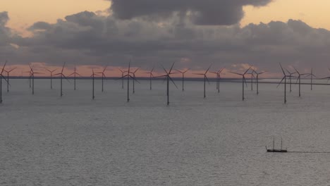 Aerial-view-of-sailing-vessel-with-In-the-background-big-windfarm-with-turbines-at-sunset,-IJsselmeer,-Netherlands