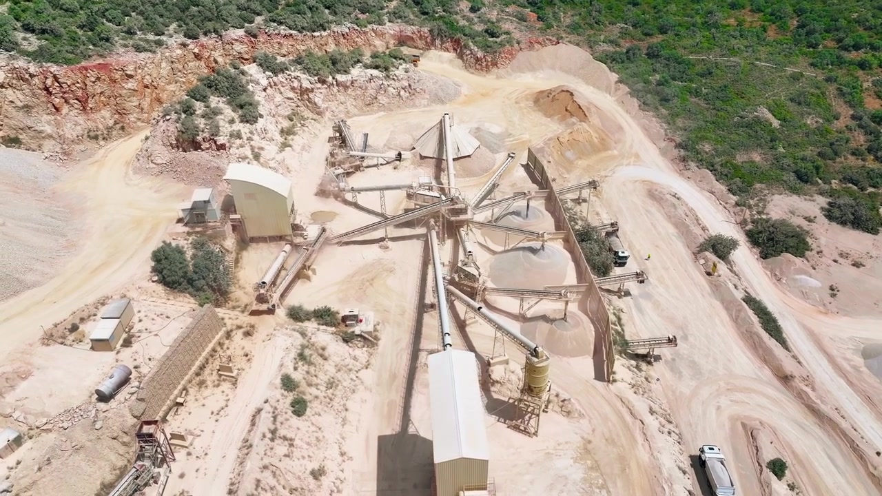 Aerial view of cement production facility with limestone quarry and aggregate processing. Heavy machinery operates in open pit mining and material handling activities.