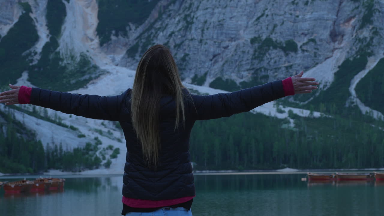 Mature woman opening her arms in front of Lago di Braies in the Dolomites