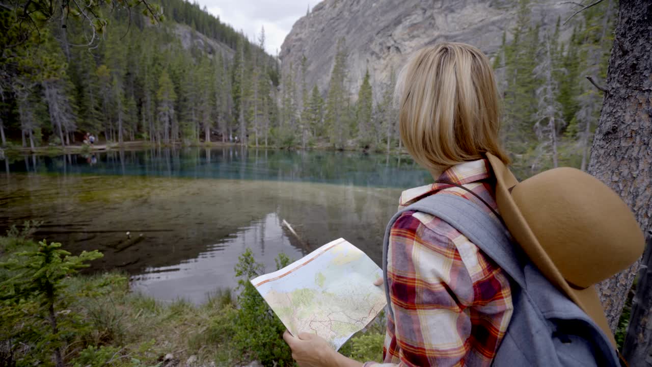 산악 호수 근처의 지도를 바라보는 하이커 여성