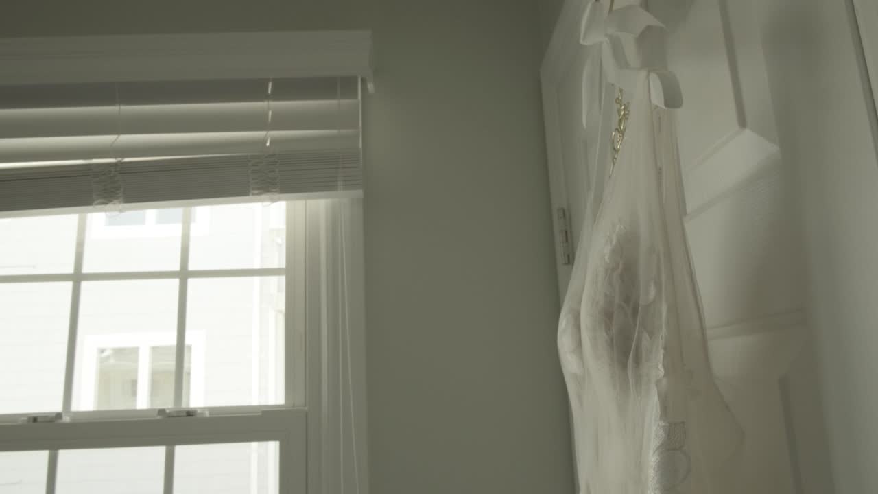 Tight Shot of a Wedding Dress Hanging Next to a Window in Bridal Suite