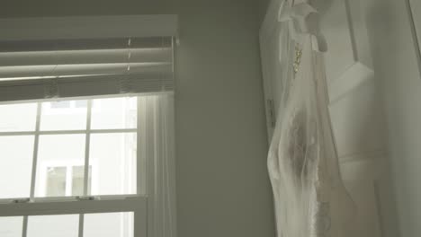 tight shot of a wedding dress hanging next to a window in bridal suite