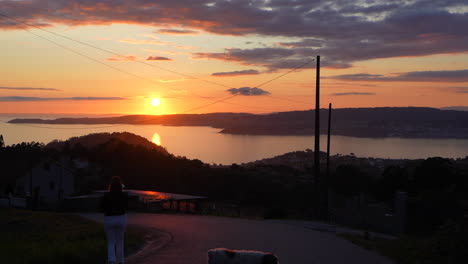 Young-woman-walking-a-coastal-road-at-sunset-with-her-dog