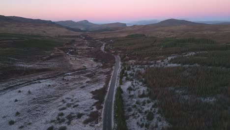 Meandering-road-through-snowy-Glencoe-at-dusk,-showcasing-the-serene-Scottish-Highlands,-aerial-view