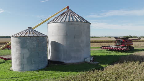 grain bin silos and combine harvester in a rural farm field, aerial