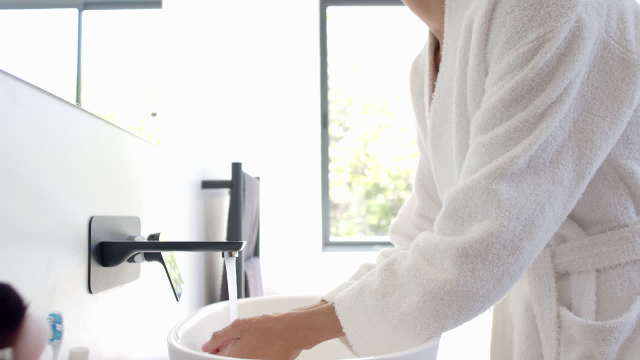 Washing face in bathroom sink, person in bathrobe enjoying morning routine