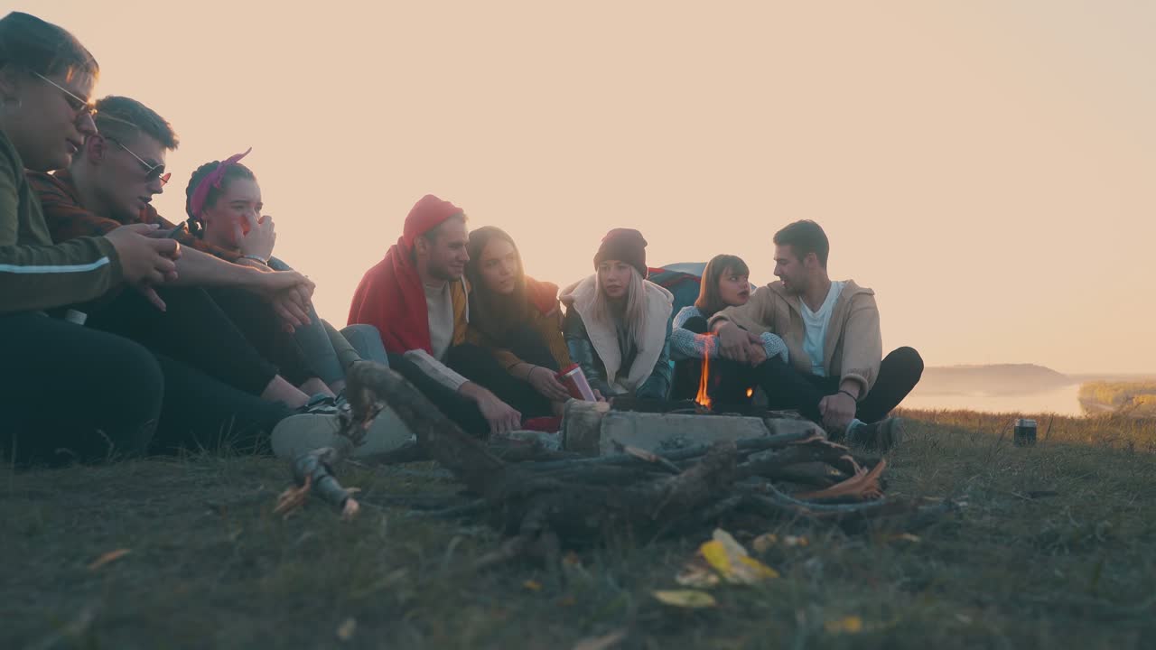 긍정적 인 친구 들 은 언덕 에 있는 강변 에서 불타는 불꽃 에 쉬고 있다