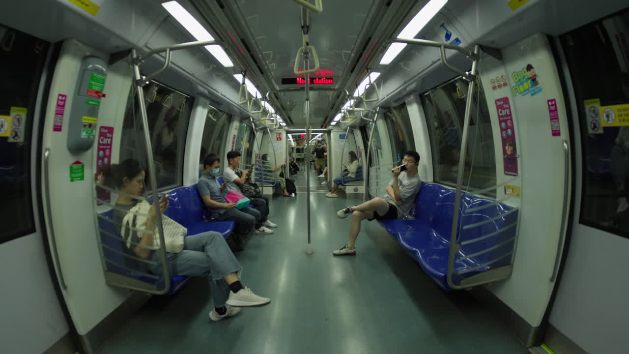 Passengers on a Singapore MRT train, some seated and using phones, while others quietly sit