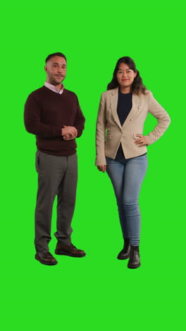 vertical video full length studio shot of smiling male and female teachers or businesspeople looking at camera against green screen