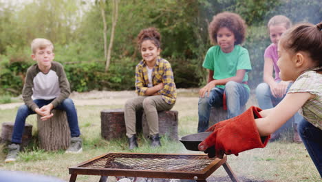 group of children on outdoor activity camping trip cooking over camp fire together