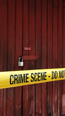 vertically filmed footage of a yellow colored crime scene do not enter police tape ribbon pulled in front of a vintage and soviet looking red garage door that is locked during day time, wind movement